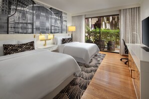 Ett hotellrum med två sängar, en stor abstrakt målning, en balkong med växter och en tv.
