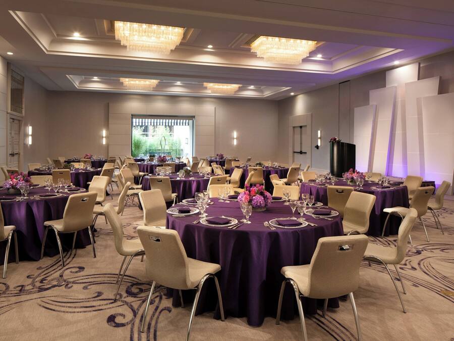 A conference room with round tables, beige chairs, purple tablecloths, and chandeliers.