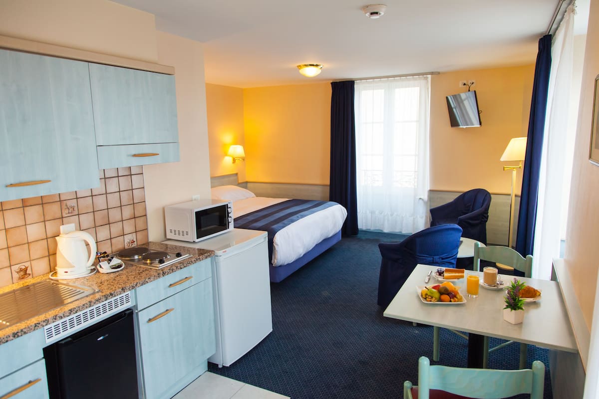 Quarto de hotel compacto com cozinha compacta, uma cama, mesa de jantar com café da manhã e uma TV presa à parede.
