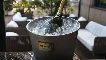 Eine Champagnerflasche in einem Metallkübel mit Eiswürfeln, beschriftet mit 'DEUTZ', auf einer Marmorplatte platziert.