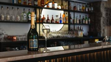Un coin bar avec une bouteille de champagne et un verre posés sur le comptoir, et des étagères remplies de différentes bouteilles en arrière-plan.