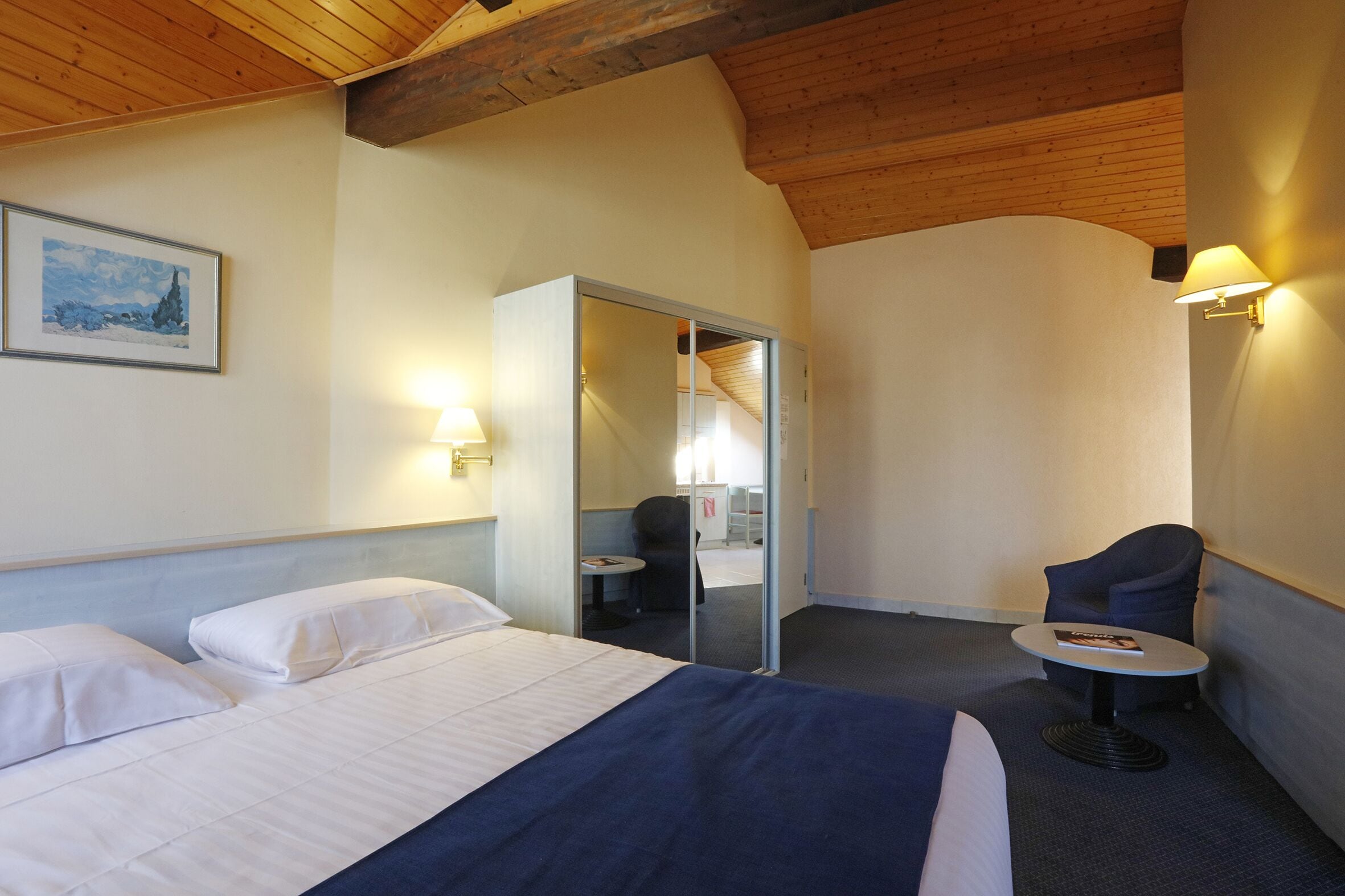 Una habitación de hotel con una cama, una silla, una mesita y un espejo.