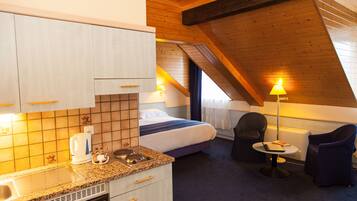 A compact hotel room with a kitchenette, a bed, a seating area, and a view of the outdoors.