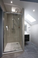 Un baño moderno con ducha de vidrio, una toalla a la vista y una lámpara en el techo.