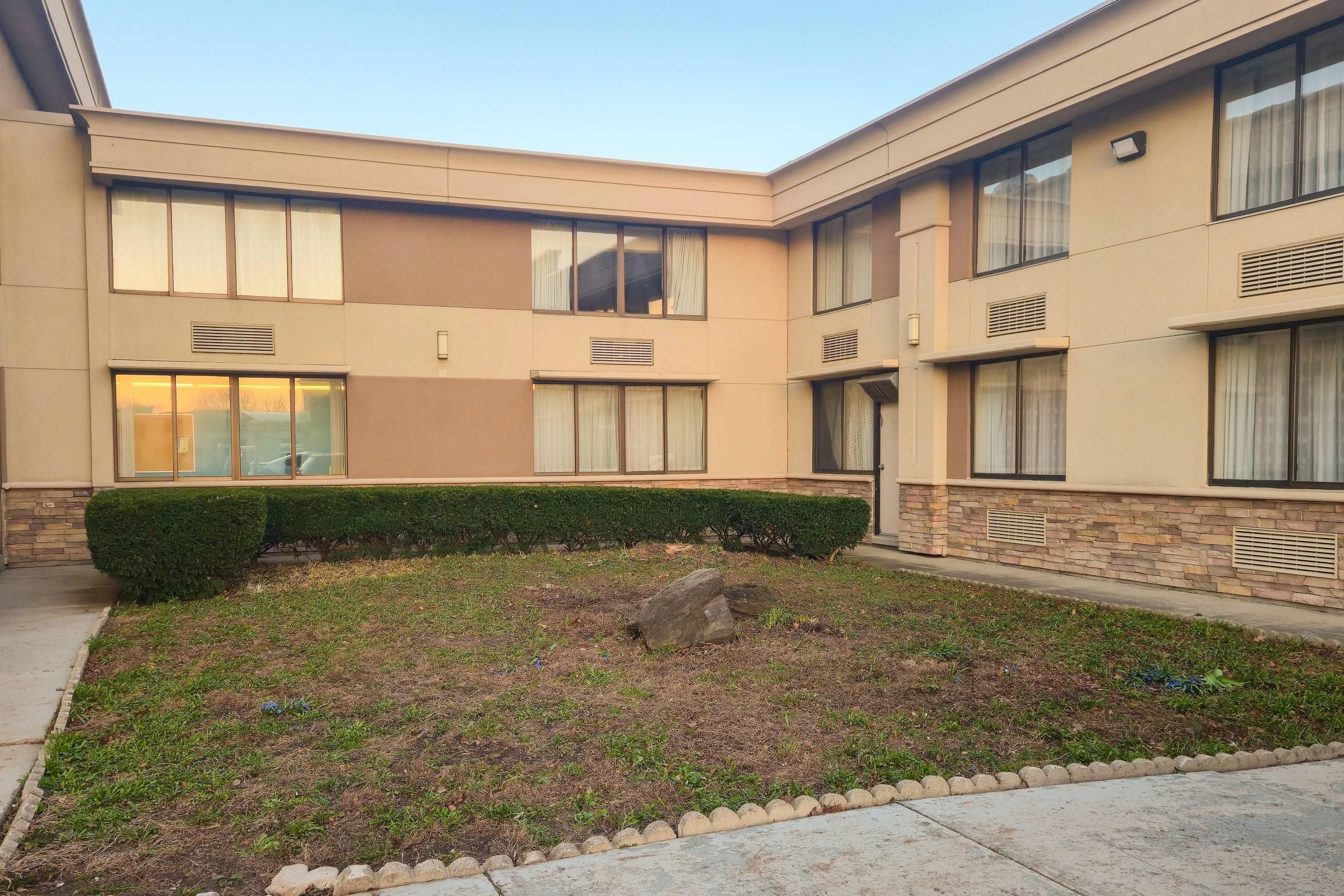 A multi-story building with a courtyard, featuring a well-maintained lawn and a hedge.