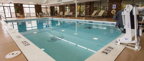 An indoor swimming pool with clear lane markings, a lifeguard chair, and lounge chairs along the poolside.