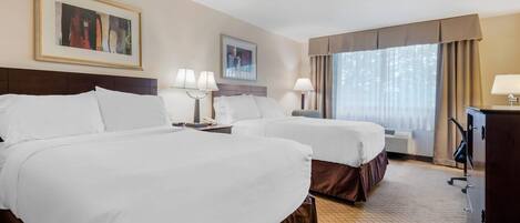A hotel room with two beds, a desk, a chair, a television, and two framed pictures on the wall.