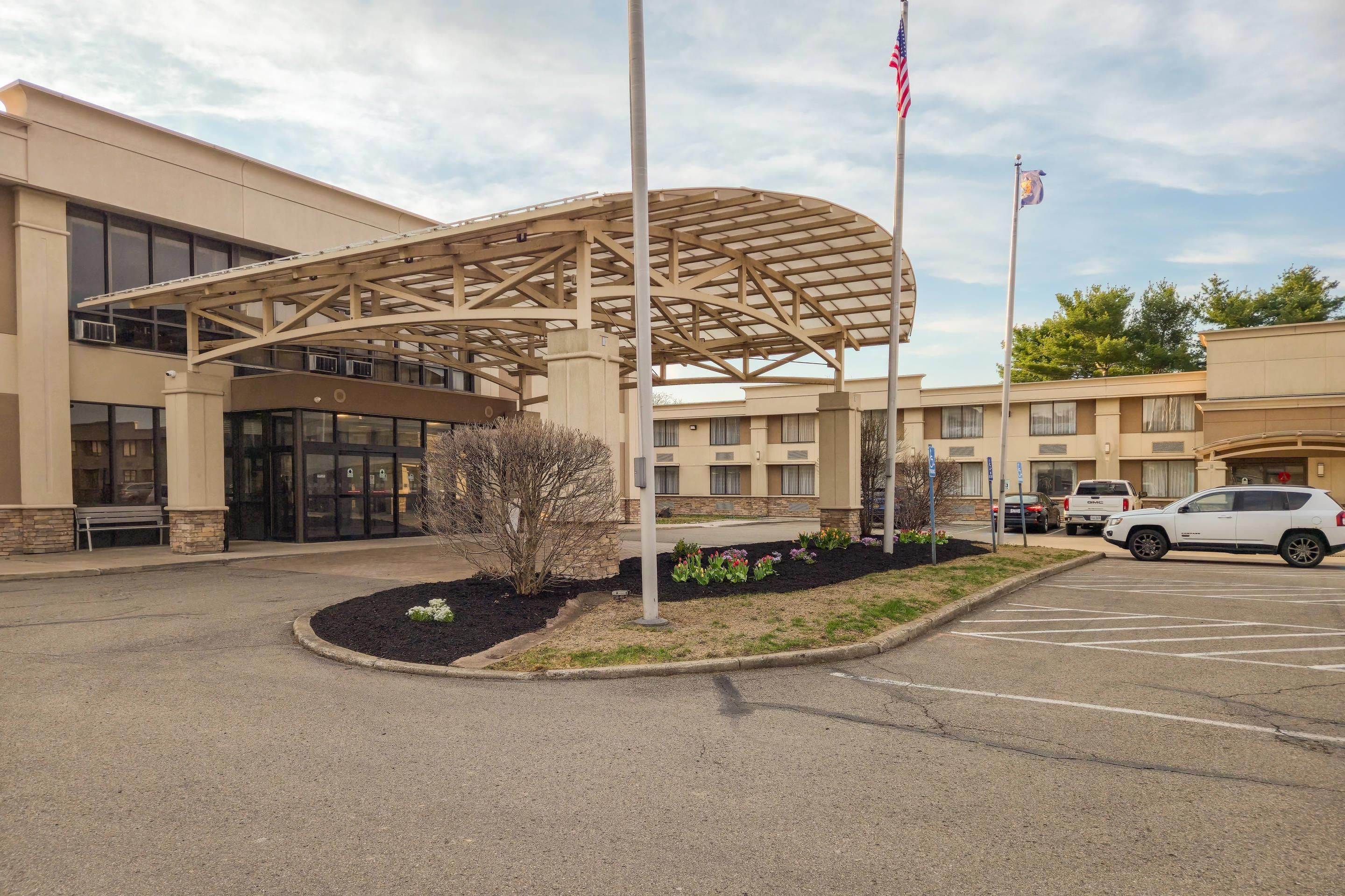 A hotel entrance with a covered walkway, a parking lot, and a flagpole.