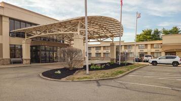 A hotel entrance with a covered walkway, a parking lot, and a flagpole.