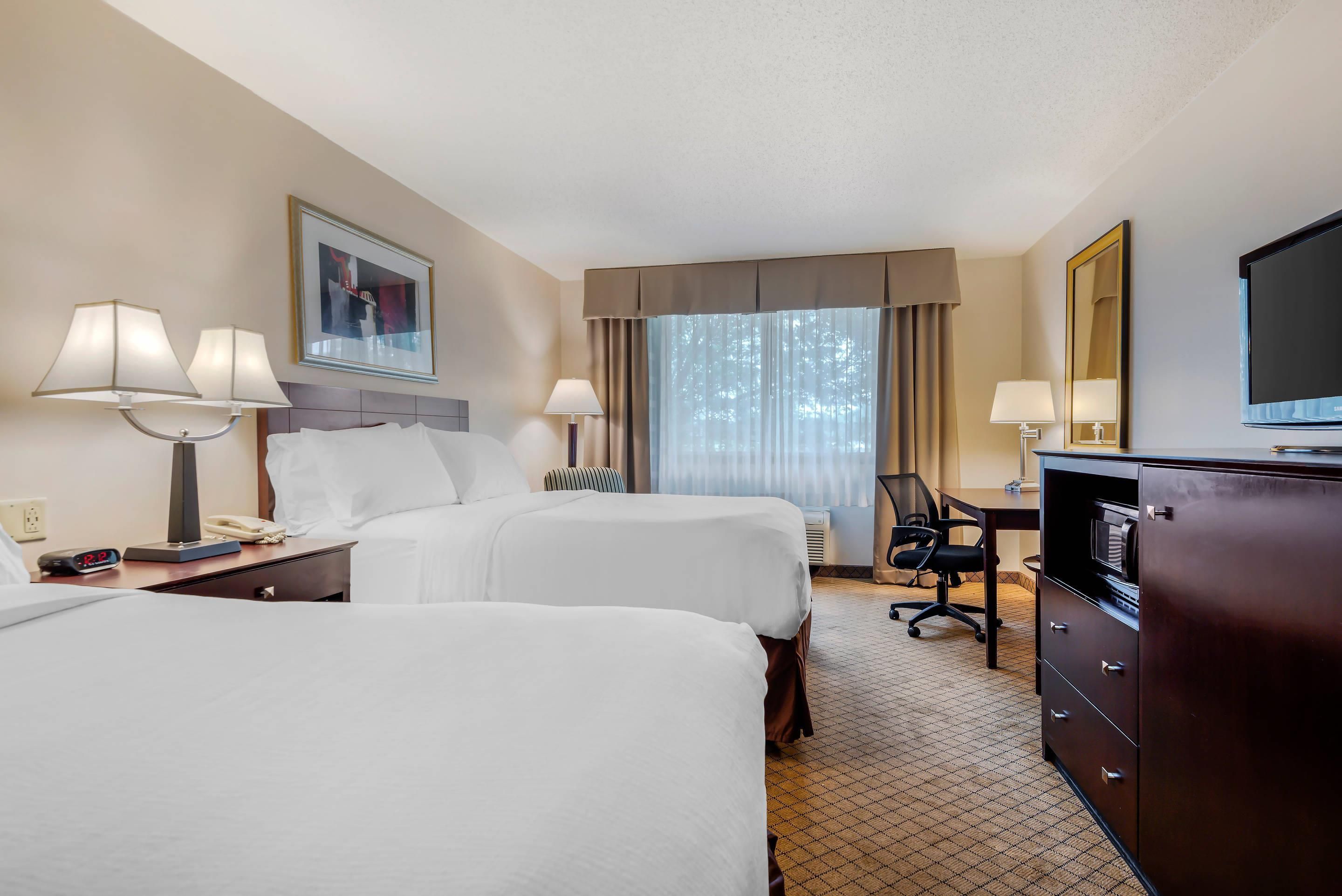 Une chambre d’hôtel avec deux lits, un bureau, une chaise, une commode, une télévision et une fenêtre avec des rideaux.