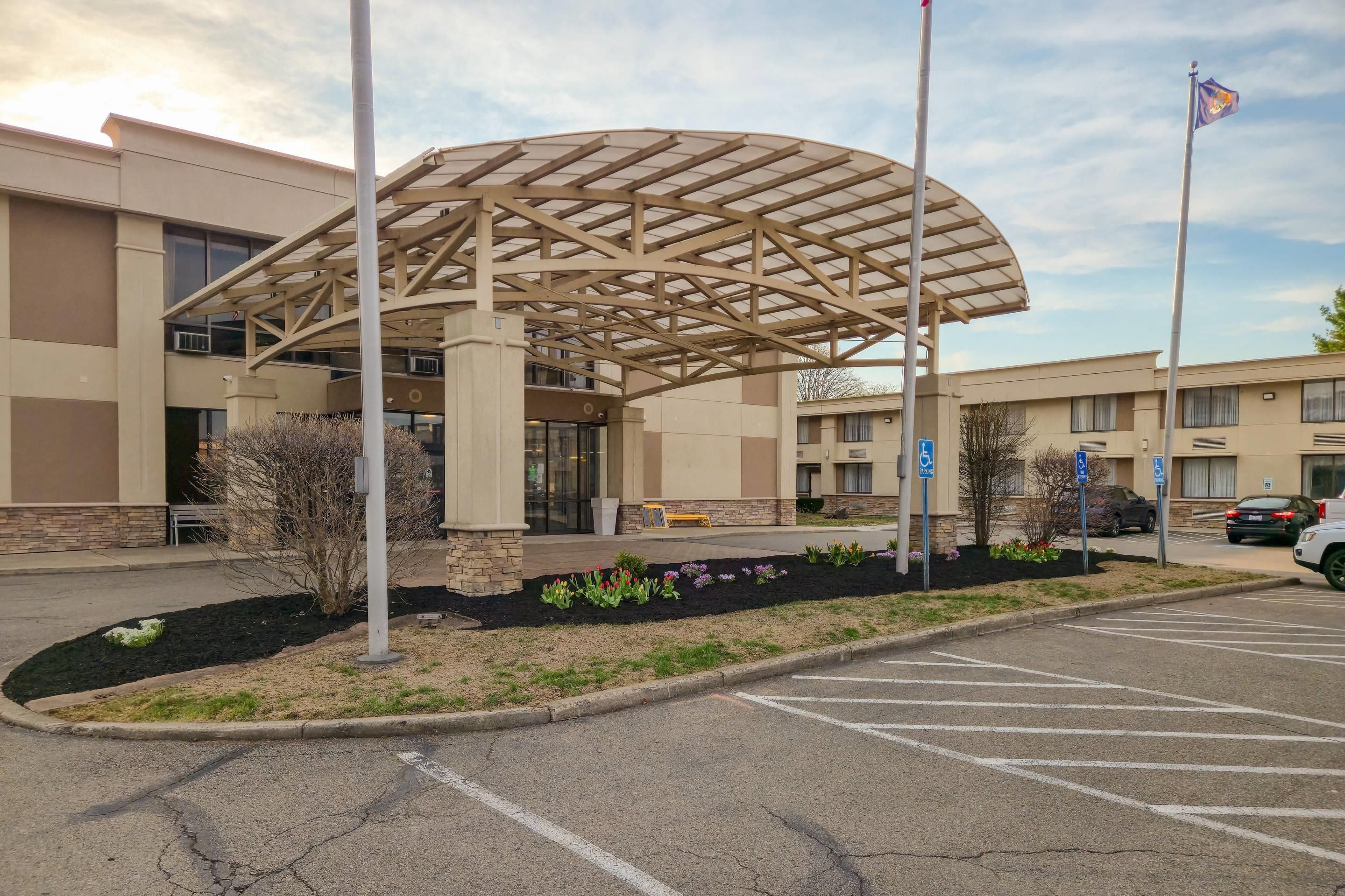 A hotel entrance with a covered waiting area, a parking lot, and a flag.
