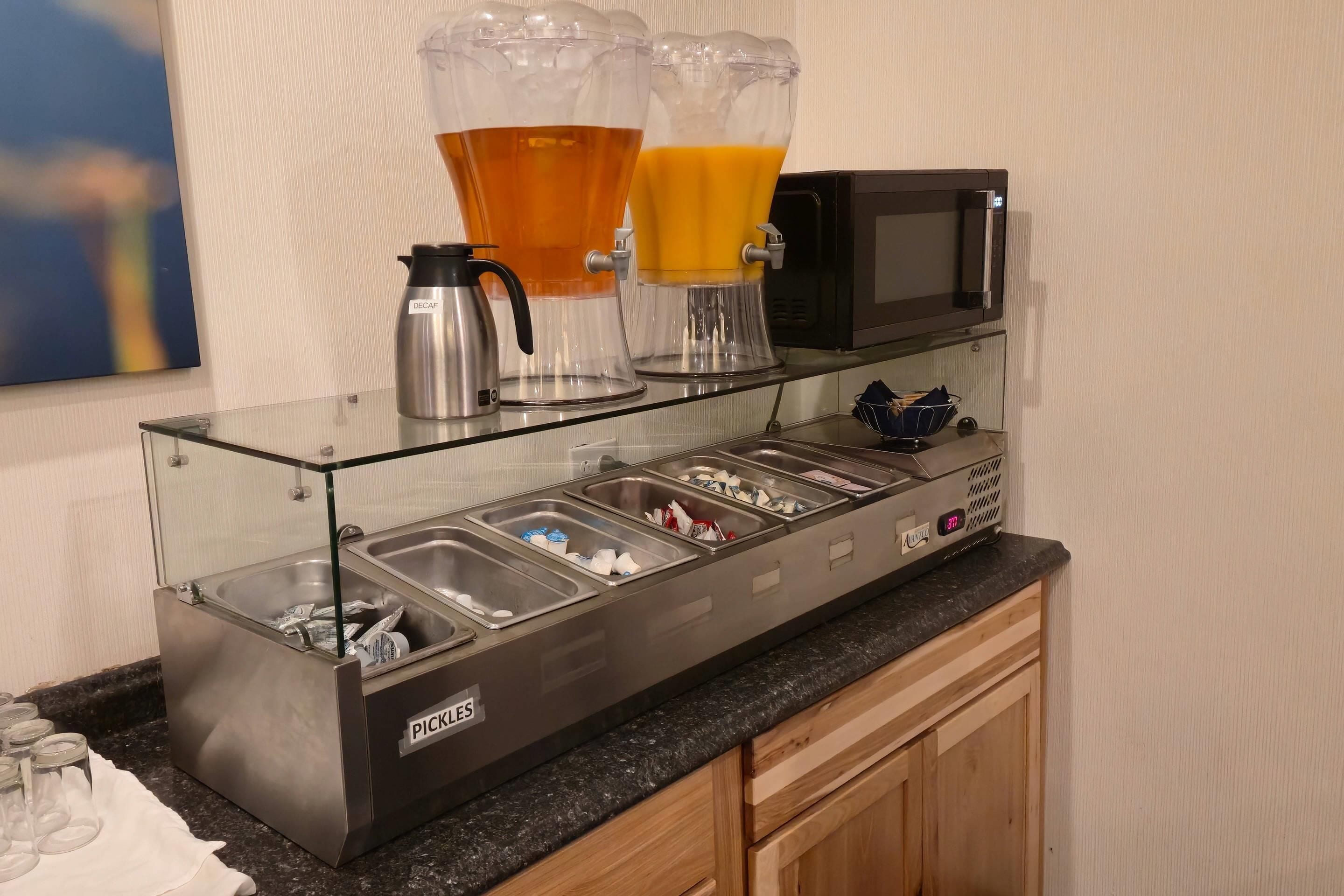 Un buffet allestito con una macchina per il caffè, due erogatori di bevande e un forno a microonde.