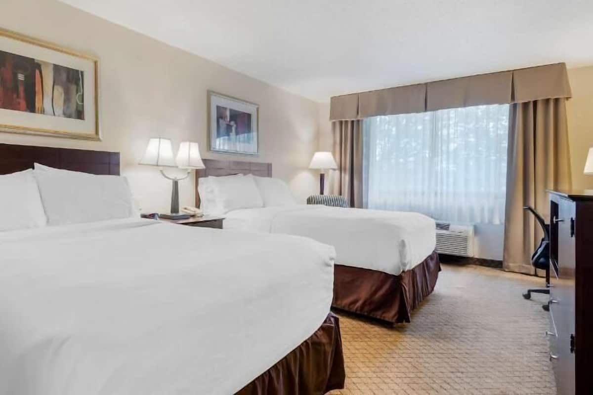 Une chambre d’hôtel avec deux lits, un bureau, une chaise et une fenêtre avec des rideaux.