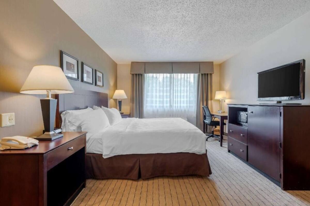 A hotel room with a bed, bedside lamps, a desk with a computer, a TV, and framed pictures on the wall.