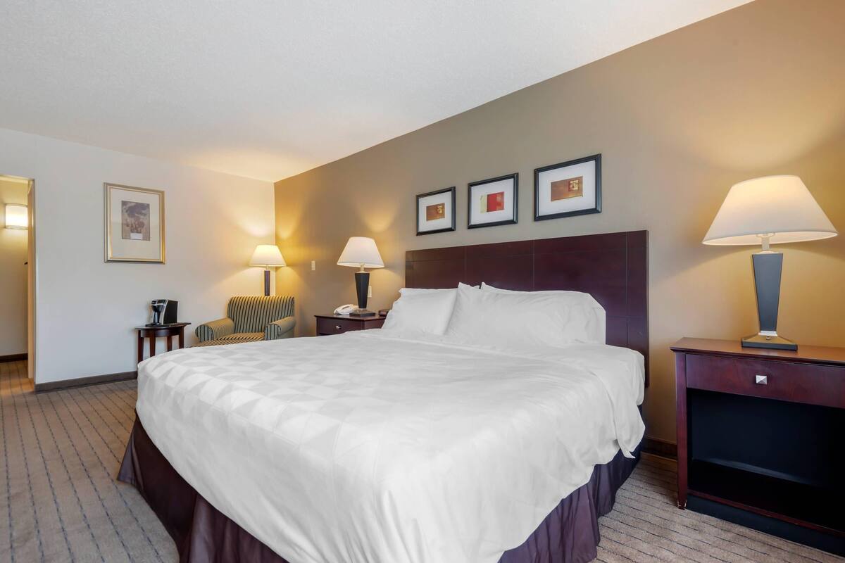 A hotel room with a large bed, two bedside tables, a chair, and a desk with a lamp.