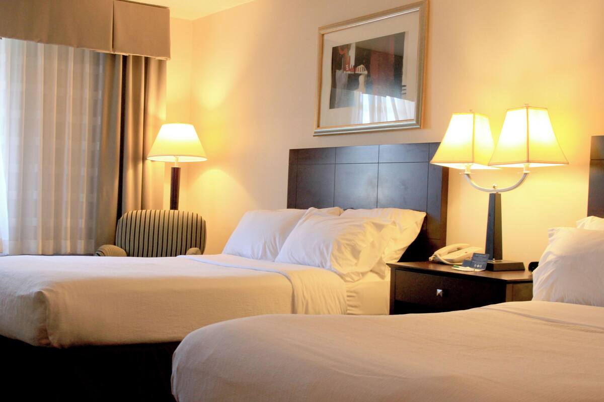 Une chambre d’hôtel avec deux lits, une tête de lit, des lampes de chevet, une table de chevet avec un téléphone et un tableau encadré au mur.