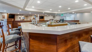 A modern bar area with a wooden counter, bar stools, and a television screen.