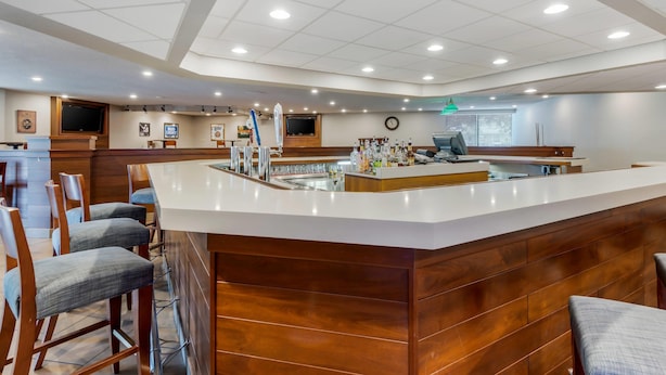 A modern bar area with a wooden counter, bar stools, and a television screen.