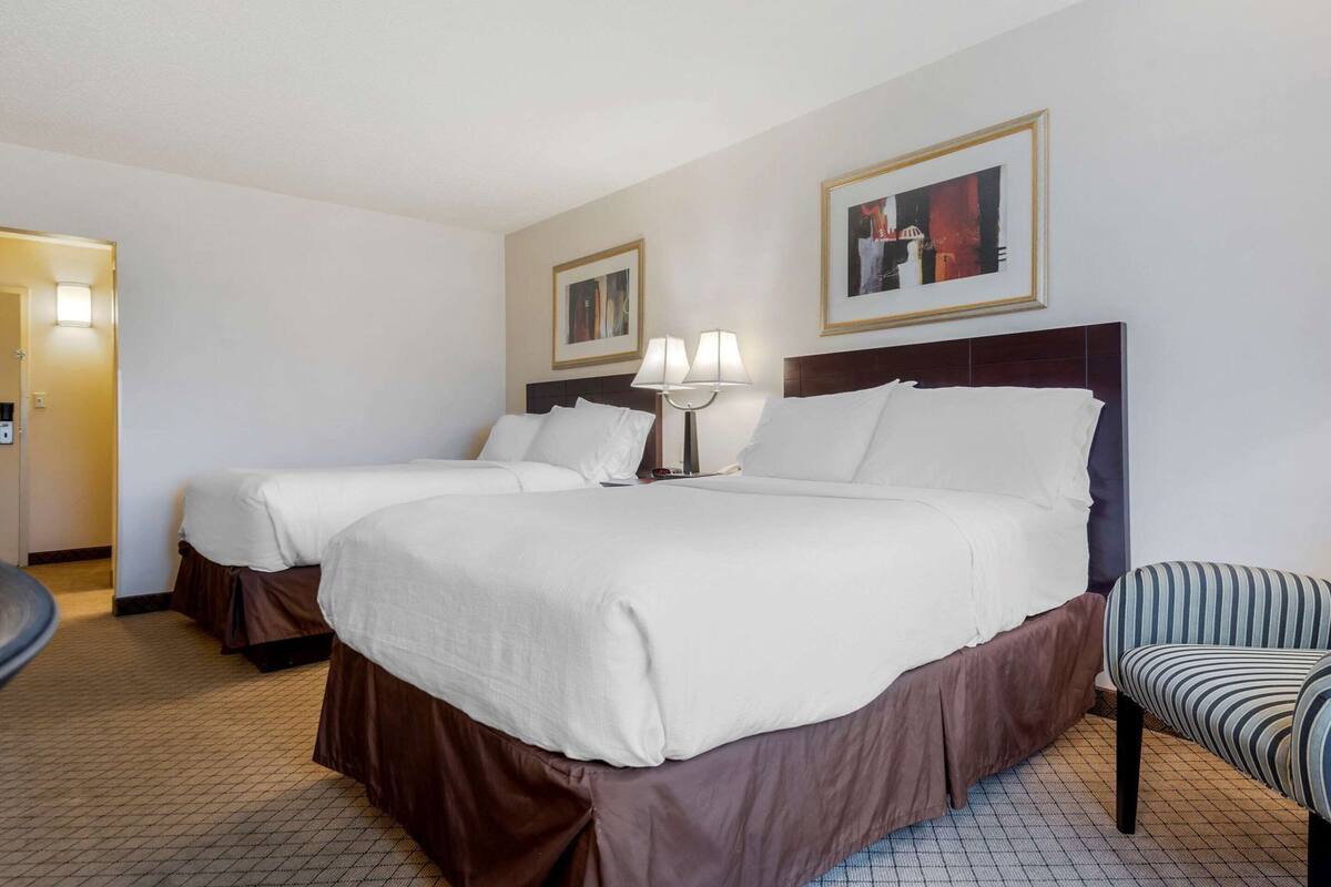 Une chambre d’hôtel avec deux lits, une chaise, une lampe et un tableau encadré au mur.