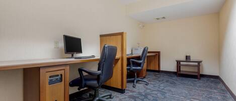 A hotel room with a desk, two chairs, a computer, a small table, and a carpeted floor.