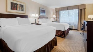 A hotel room with two beds, a desk, a chair, a television, and two framed pictures on the wall.