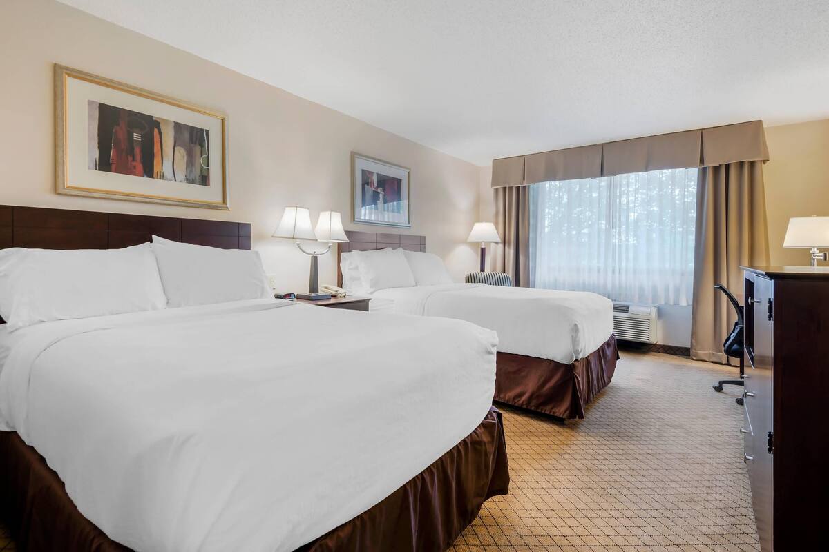 A hotel room with two beds, a desk, a chair, a television, and two framed pictures on the wall.