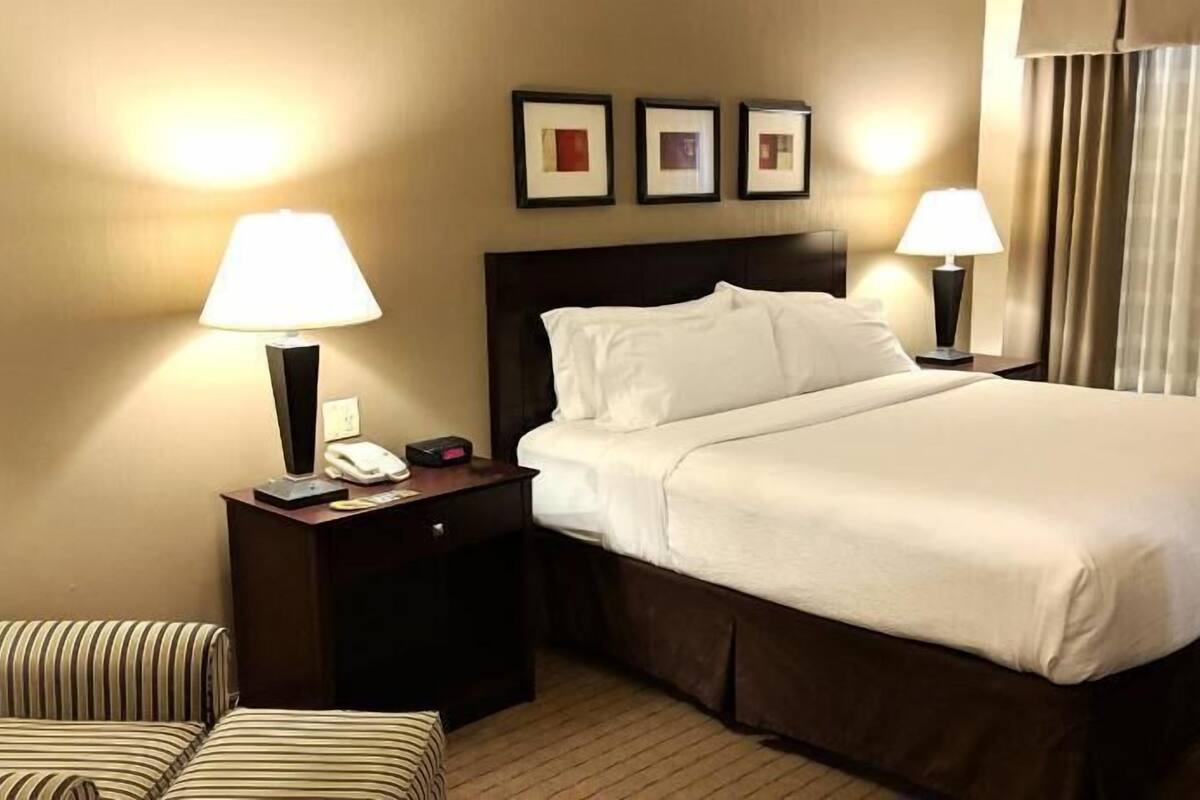 A hotel room with a bed, two bedside lamps, a telephone, a clock, and a chair.