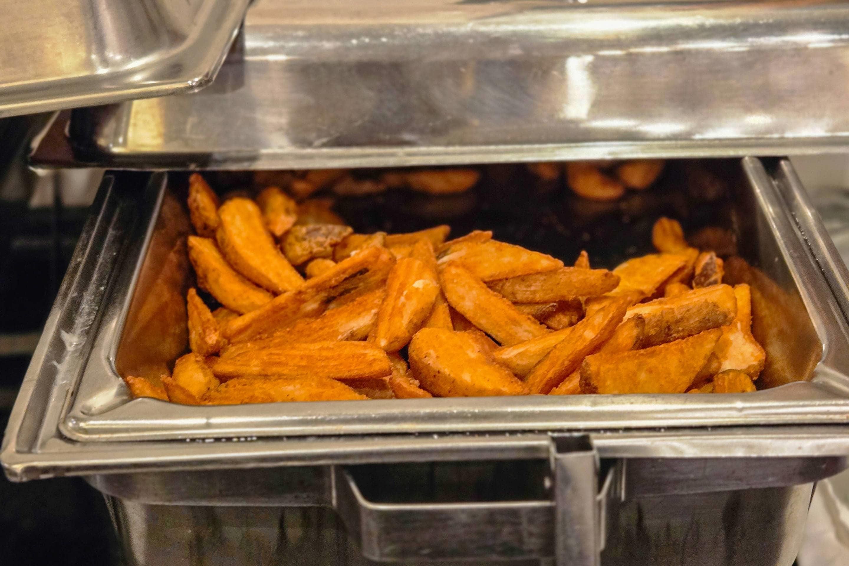 A buffet with a metal container filled with golden-brown french fries.