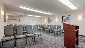 Een vergaderzaal met rijen stoelen, een spreekgestoelte en verlichting in het plafond.