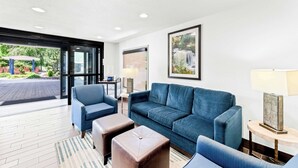 A modern hotel lobby with a blue sofa, two ottomans, a coffee table, and a framed picture on the wall. - Comfort Inn near Great Smoky Mountain National Park (Maggie Valley)