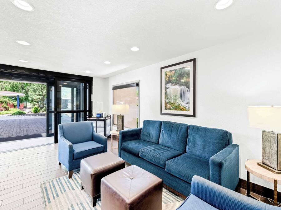 Un hall d’hôtel moderne avec un canapé bleu, deux poufs, une table basse et un tableau encadré au mur.