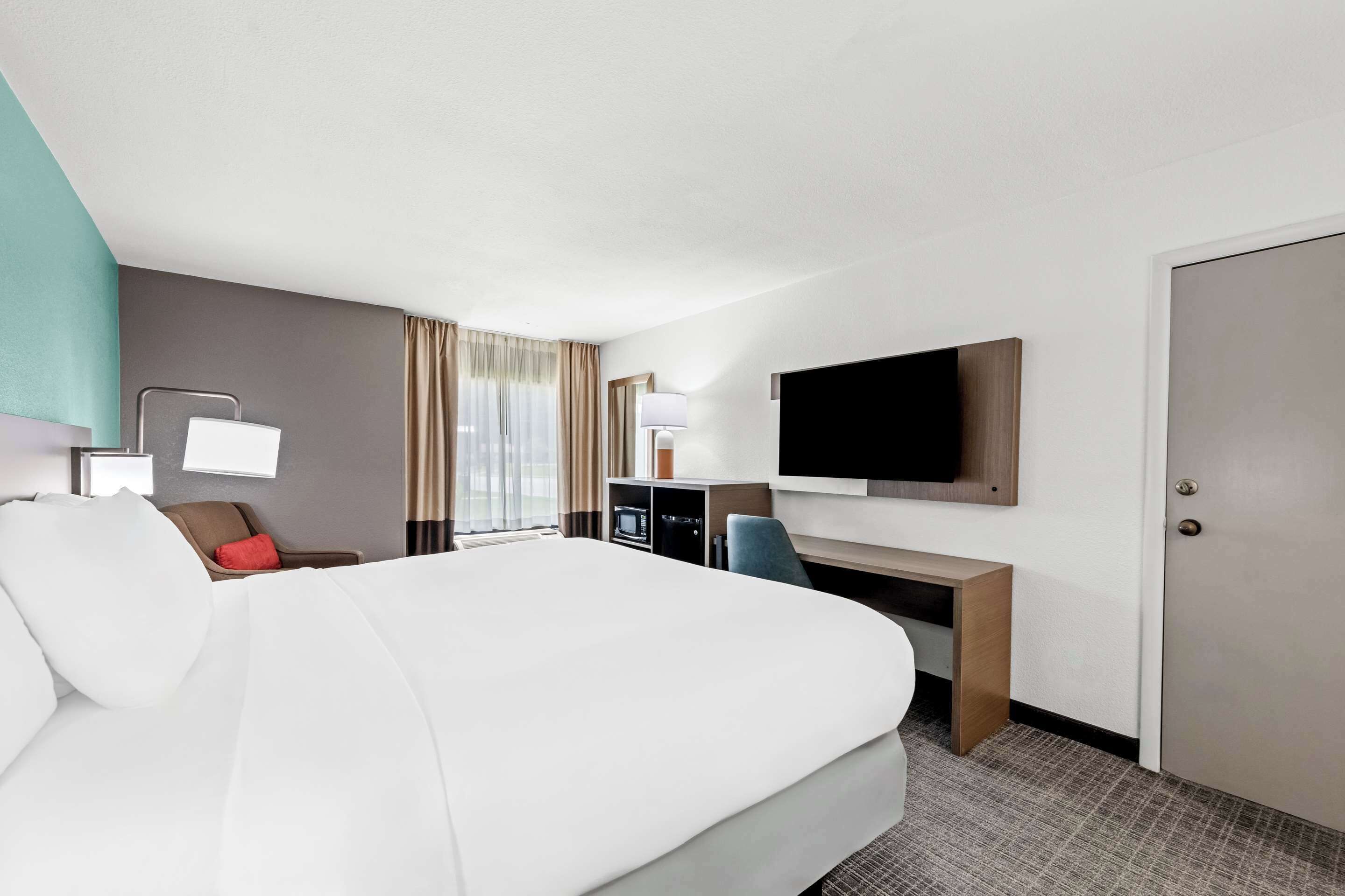 Habitación de hotel con una cama grande, un escritorio con televisión de pantalla plana, una silla, una lámpara de escritorio y un armario.