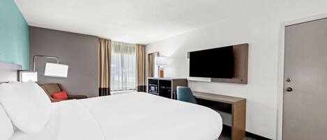 Habitación de hotel con una cama grande, un escritorio con televisión de pantalla plana, una silla, una lámpara de escritorio y un armario.