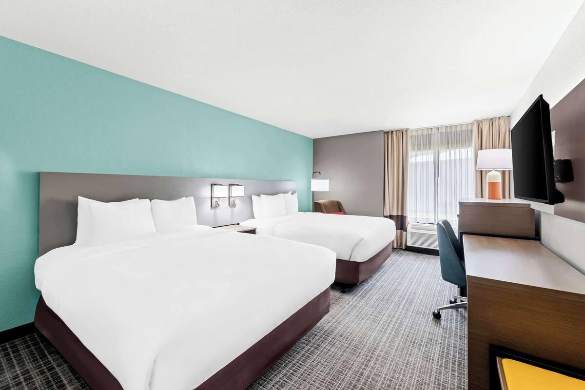 A hotel room with two beds, a desk, a chair, a TV, and a window with curtains.