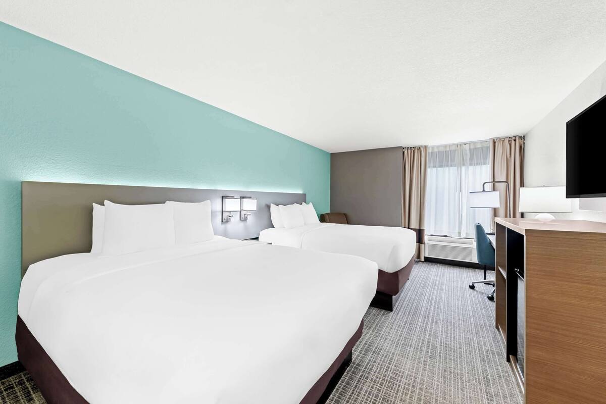 A hotel room with two beds, a desk, a TV, and a window with curtains.