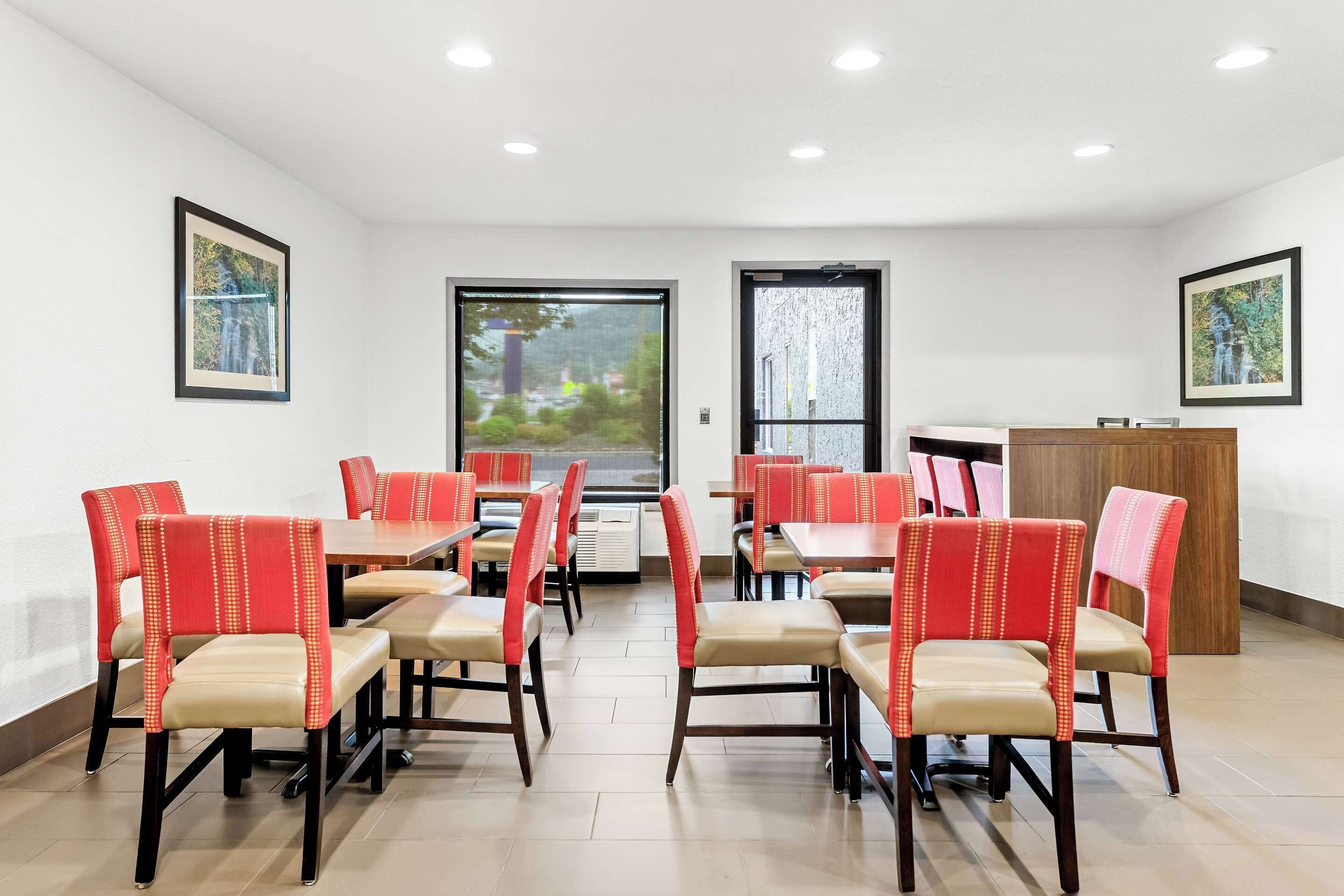 A dining area with red and beige chairs, tables, and a wooden cabinet.