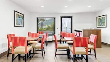 A dining area with red and beige chairs, tables, and a wooden cabinet.