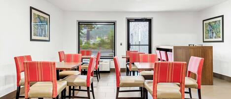 A dining area with red and beige chairs, tables, and a wooden cabinet.