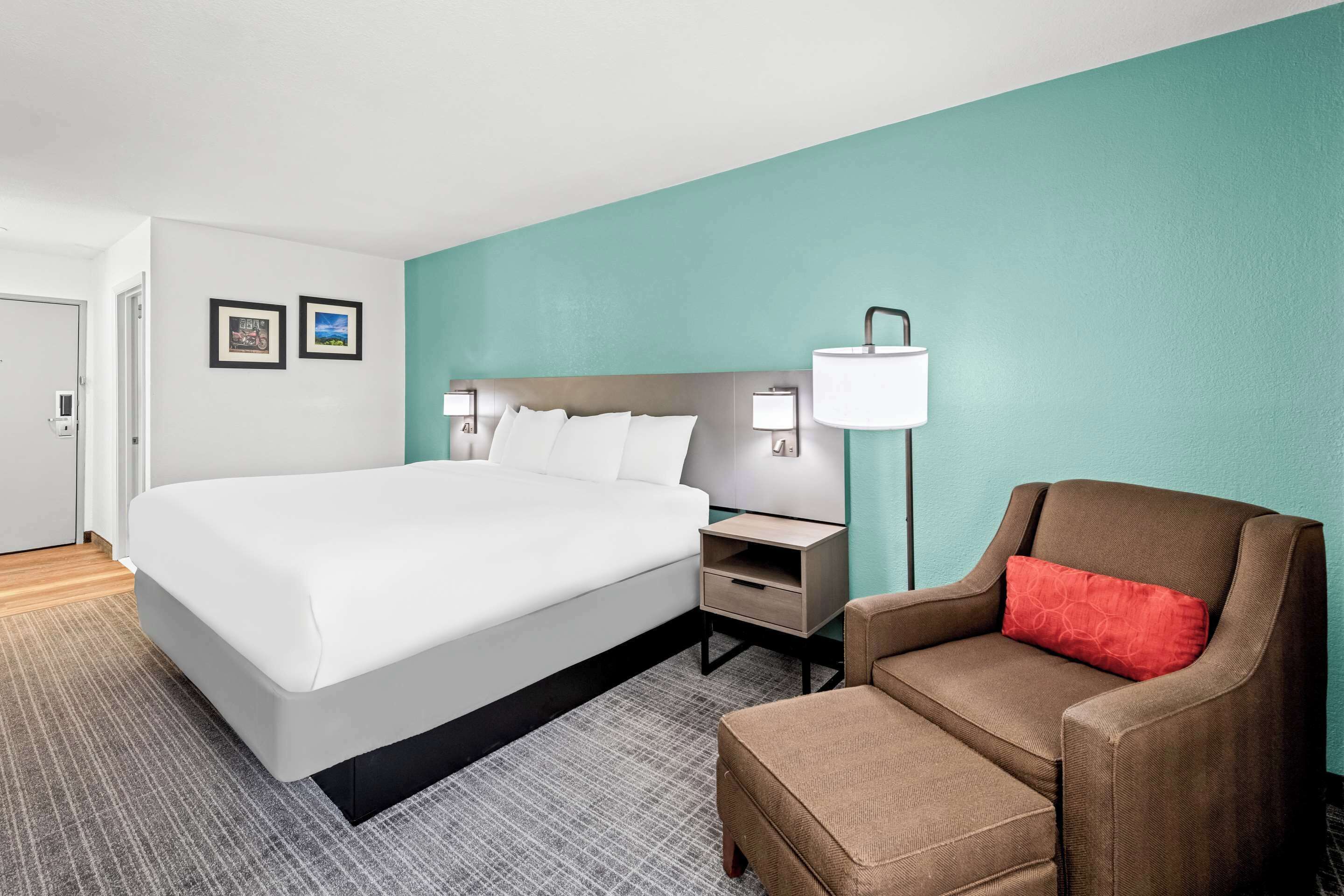 A hotel room with a large bed, a nightstand, a lamp, a chair, and two framed pictures on the wall.