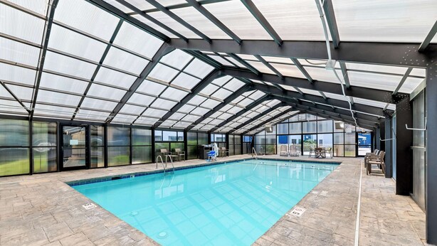 An indoor swimming pool with a glass ceiling, tiled floor, and seating area. - Comfort Inn near Great Smoky Mountain National Park (Maggie Valley)