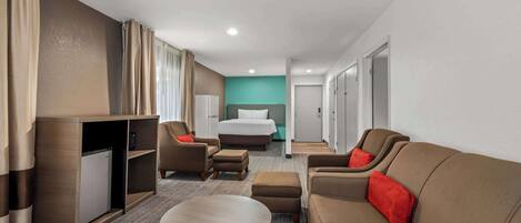 A hotel room with a bed, a sofa, a coffee table, a desk with a computer, and a wardrobe.