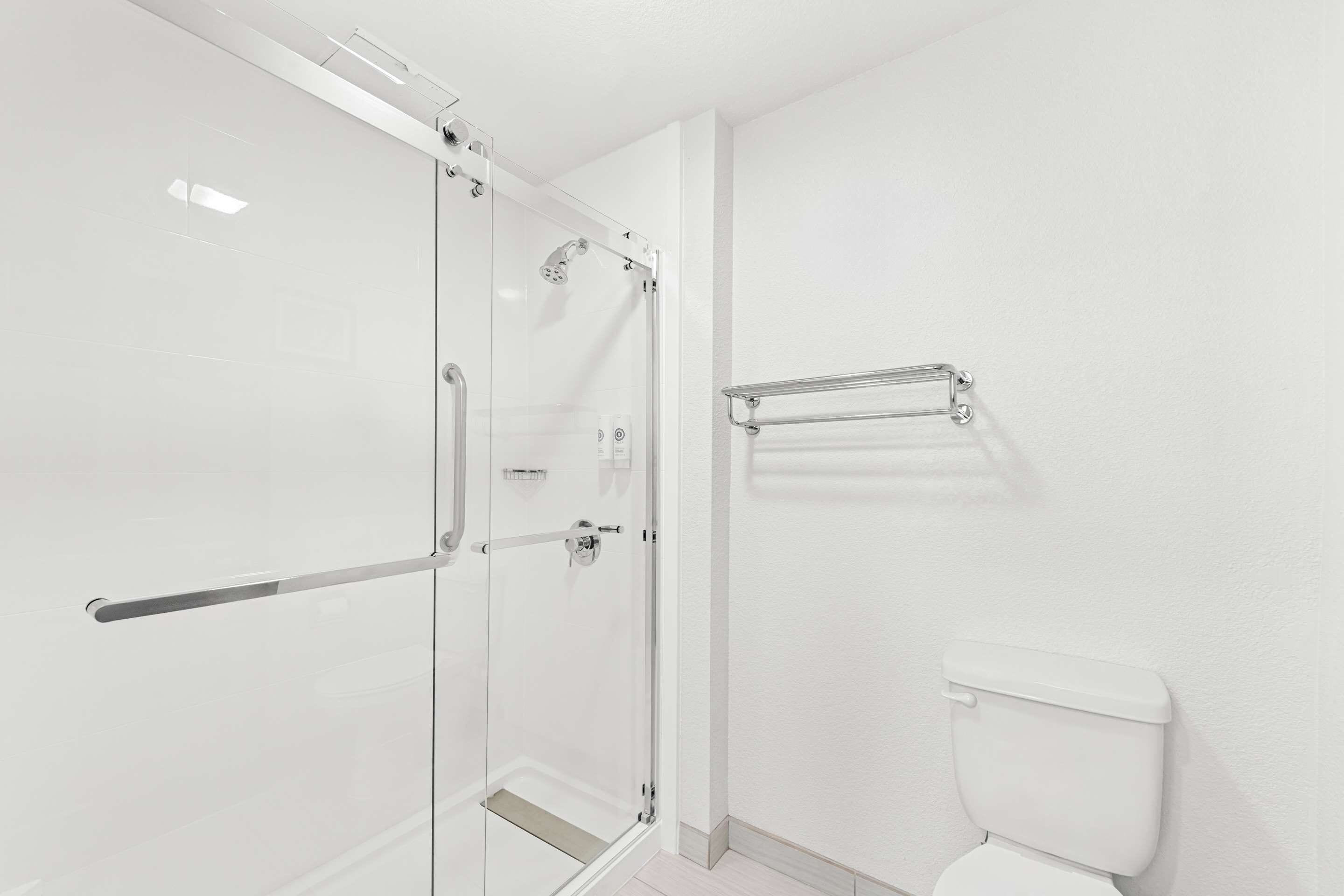 A modern bathroom with a glass shower enclosure, a white toilet, and a towel rack.