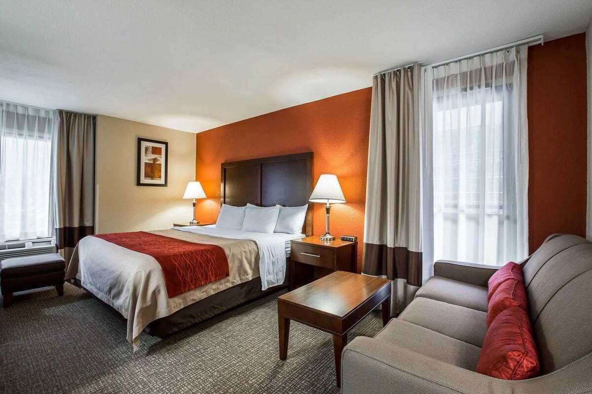A hotel room with a bed, two bedside tables with lamps, a sofa, and a carpeted floor.