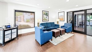 A modern hotel room with a large window, a blue sofa set, a small table, and a cart with a laptop. - Comfort Inn near Great Smoky Mountain National Park (Maggie Valley)