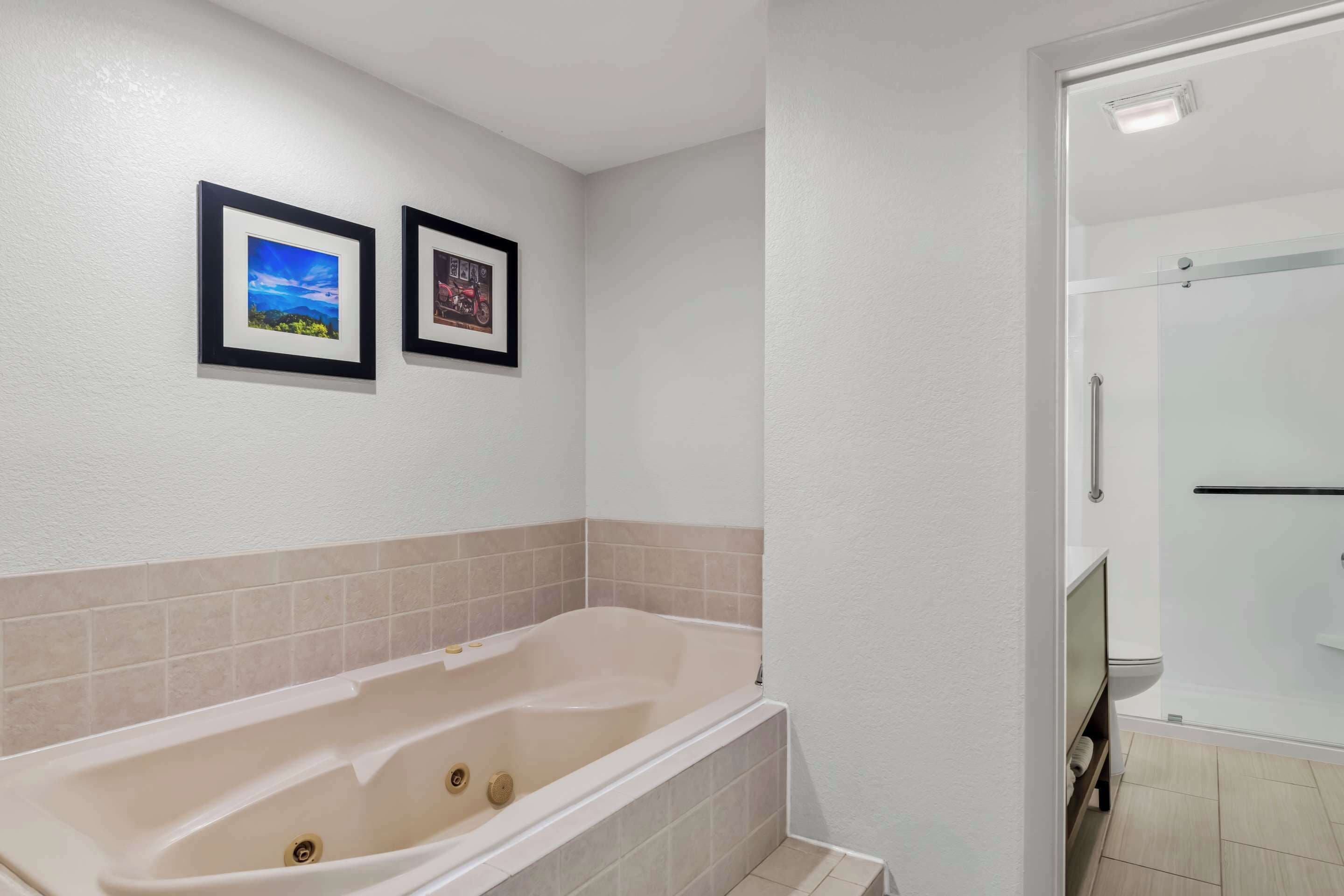 A bathroom with a bathtub, a toilet, and a shower area. There are two framed pictures on the wall.