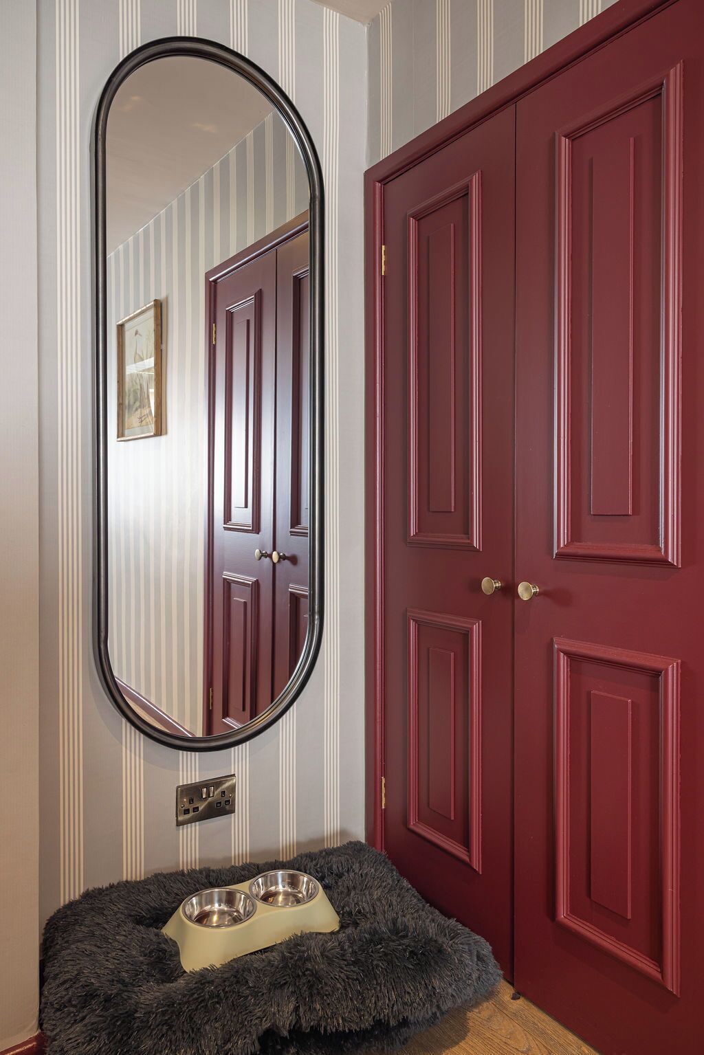 Una habitación con un espejo grande, una puerta roja y una cama para mascotas con platos.