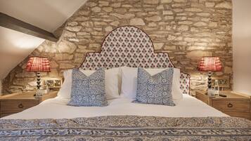 Een slaapkamer met een stenen muur, een bed met beddengoed met een patroon, en twee bedlampen.