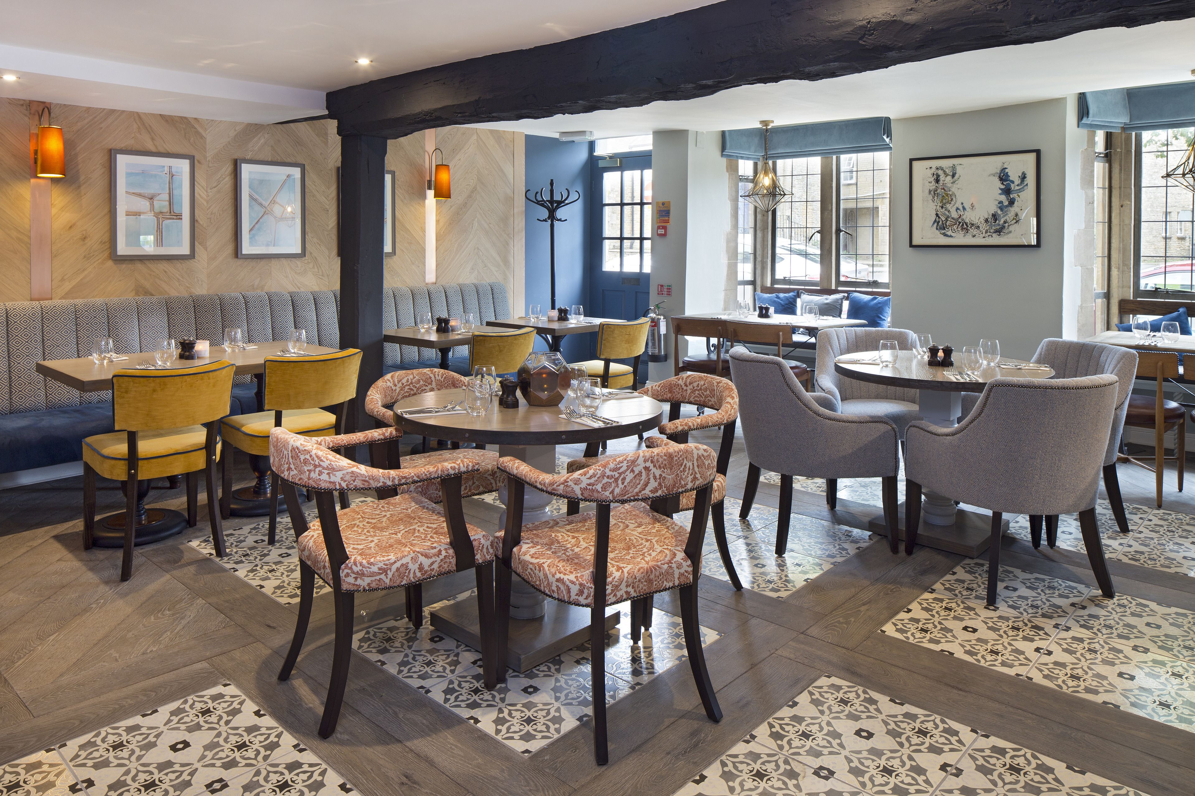 A restaurant interior with multiple dining tables and chairs, a patterned floor, and artwork on the walls.
