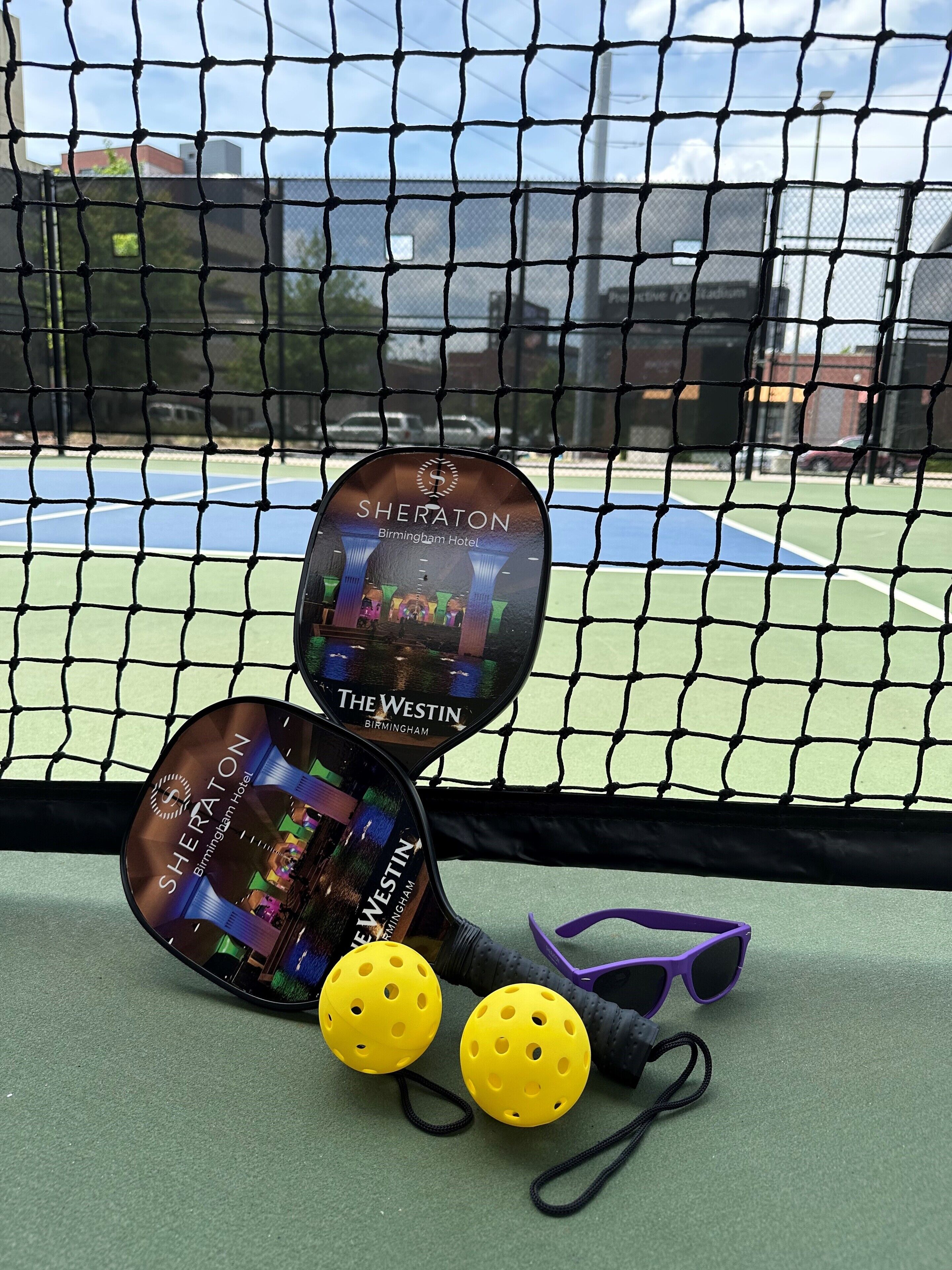 A tennis court with a net, two tennis rackets, and two yellow tennis balls.