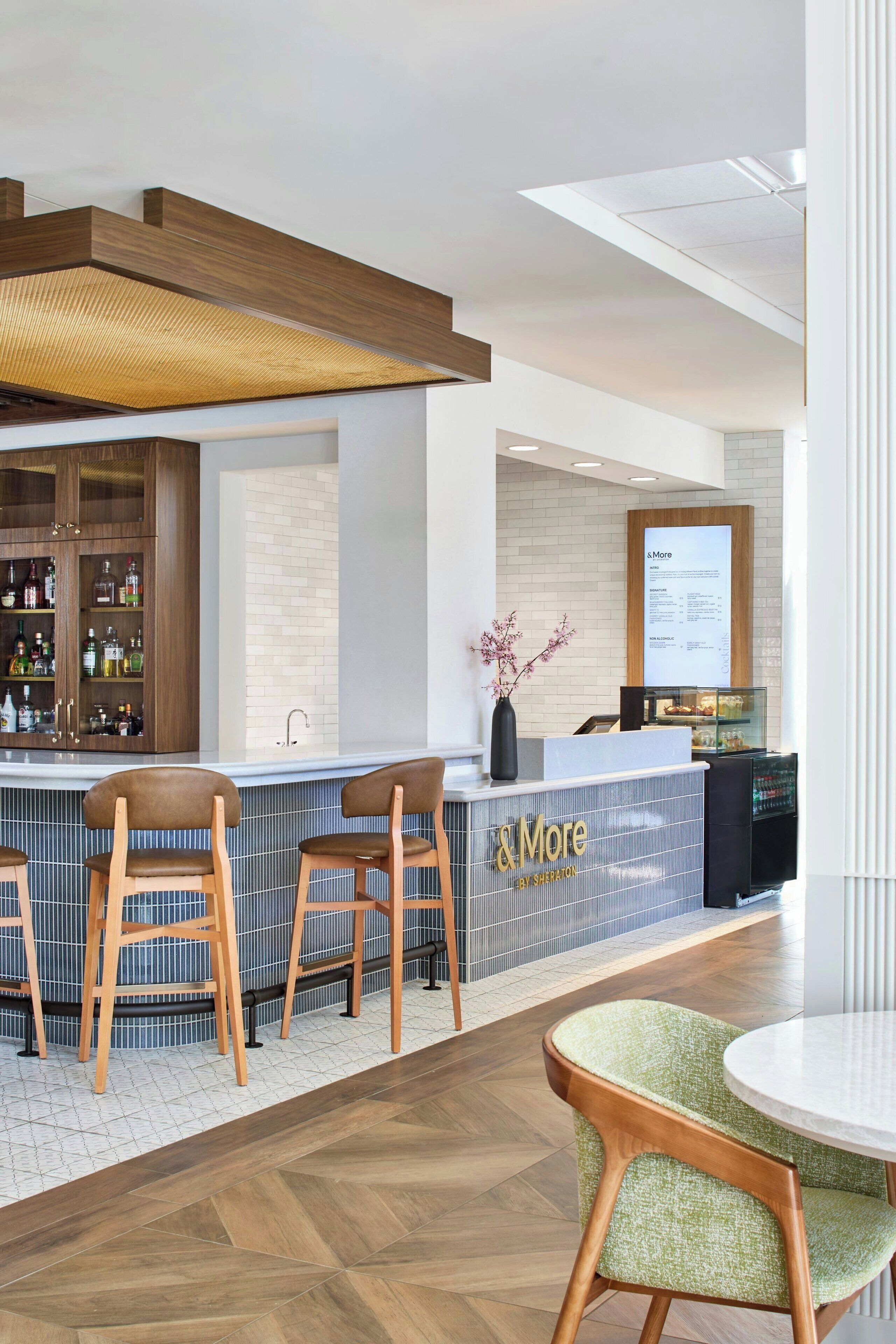 A modern bar area with wooden bar stools, a counter with a menu display, and a tiled floor.